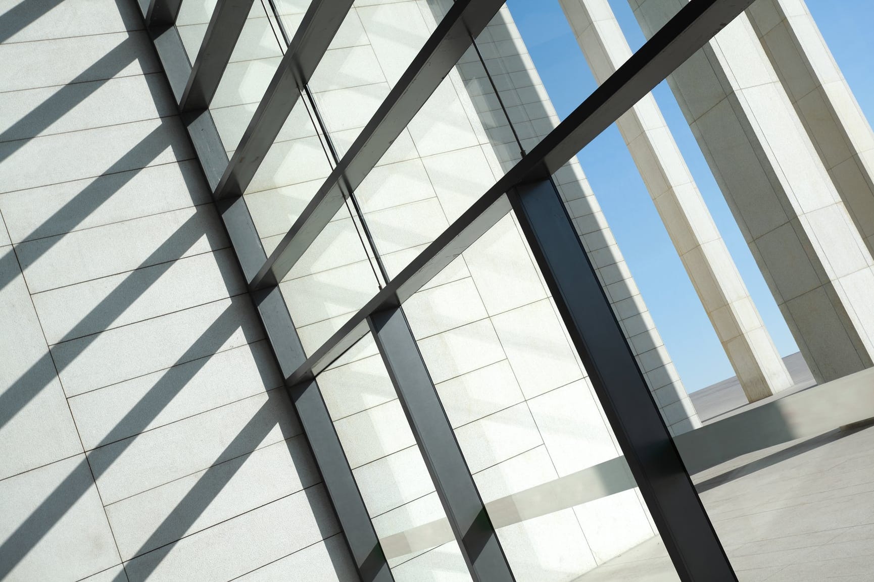 Architectural detail of a concrete and metal building, window with blue sky visible on right side.